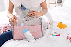 Woman packing baby accessories into maternity bag on bed