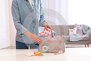 Woman packing baby accessories into maternity bag on table indoors