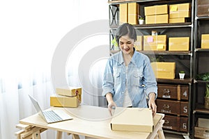 Woman packing box on table checking goods package delivery shipping to customer. Asian woman startup small business at home office