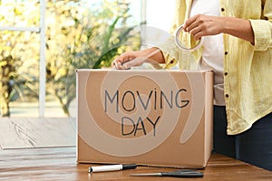 Woman packing box with words MOVING DAY at table, closeup
