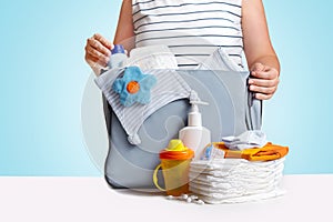 Woman packing diaper bag on blue background.