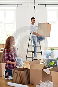 Woman packing stuff and man with painting on ladder in blurred background moving out from home