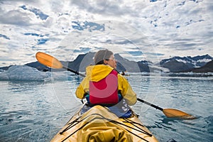 Woman paddle a canoe on an icy bay in Alaska exploring glaciers.