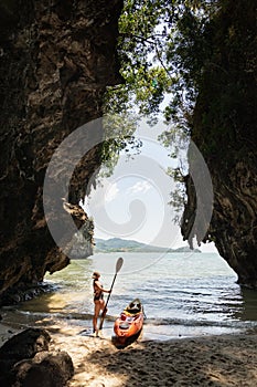 Woman with a paddle standing next to sea kayak at secluded beach in Krabi, Thailand