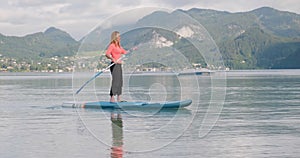 Woman paddles on sup board at Wolfgang mountain lake, Austria, early morning. Active tourism and travel, water sport during summer