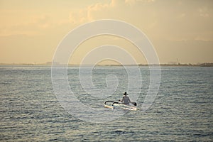 Woman in hat paddling on canoe in sunset ocean