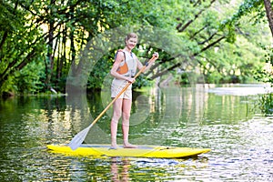 Woman paddling with surfboard sup on forest river