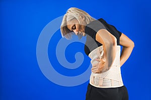 Woman in pain from back injury wearing lumbar brace corset on a blue background