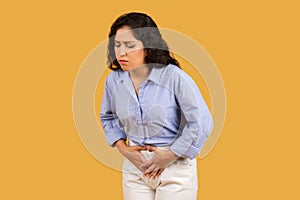 Woman with a pained expression, clutching her abdomen, possibly experiencing stomach pain