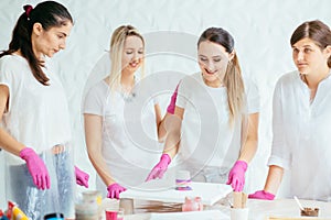 Woman painter holding hair dryer while female beginnres studying creating fluid acrylic abstract painting in art therapy