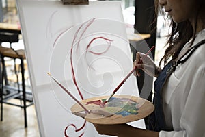 Woman painter holding painting brush and palette painting on canvas at in art studio.