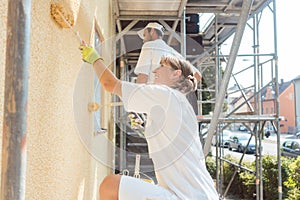 Woman painter painting a wall with yellow paint