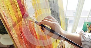 Woman painter's hand with brush painting abstract picture on canvas on easel.