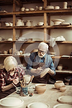 Woman painting clay pot with senior potter