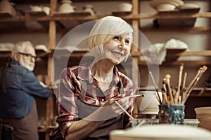 Woman painting clay pot with senior potter