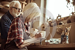 Woman painting clay pot with senior potter