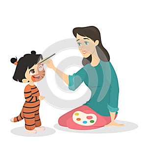 Woman painting the face of the girl in the tiger costume