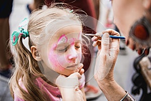 Woman painting face of kid outdoors photo