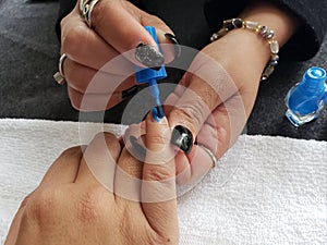 woman painting the fingernails of another woman with blue nail polish photo