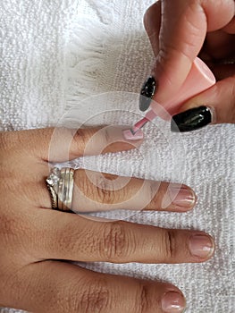 woman painting the fingernails of another woman with pink nail polish photo