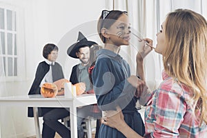 A woman is painting on the girl`s face a make-up of a kitten for a party on Haloween