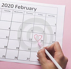 Woman painting heart on Date February 14 on calendar