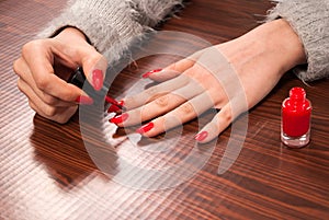 Perfectly Polished: Young Woman Painting Her Nails in Red on a Wooden Desk