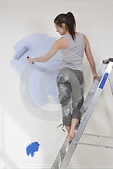 Woman Painting Wall With Paintroller While Standing On Stepladder