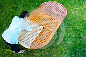 Woman painting wooden exotic wood table in the garden with a brush