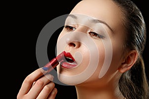 A woman paints her lips with red lipstick