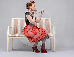 Woman paints lips with lipstick sitting on a couch in nature.