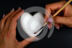 A woman paints a white heart with red paint. Love symbol Black background