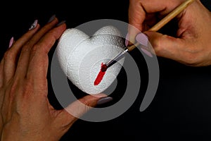 A woman paints a white heart with red paint. Love symbol Black background