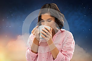 Woman in pajama drinking coffee from mug at night