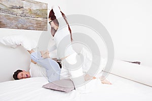 Woman in pajamas hitting man with pillow while he