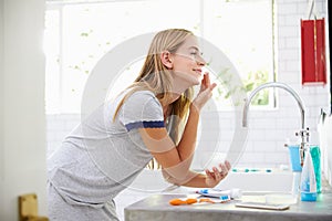 Woman In Pajamas Putting On Moisturizer In Bathroom