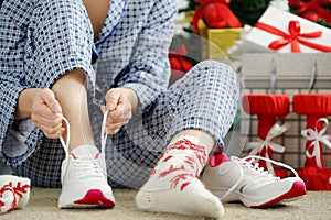 Woman in pajamas ties the laces of athletic shoes.