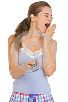 Woman in pajamas with TV remote control yawing