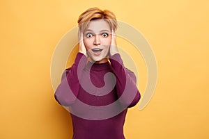 Woman with palms on her head and wide open mouth looking at camera