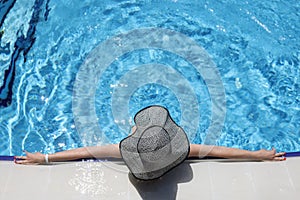 Woman in panama lying on edge of swimming pool top view