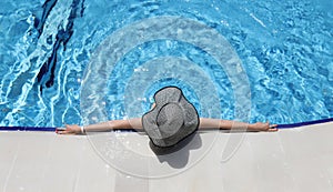 Woman in panama lying on edge of swimming pool top view