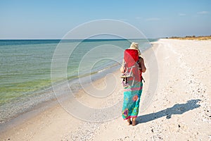 Woman in a pareo with backpack goes along deserted beach