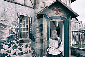 A woman parishioner in a headscarf stands and crosses herself at the door of a retro american church