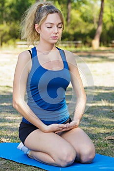 woman in park kneeling with closed eyes on yoga mat