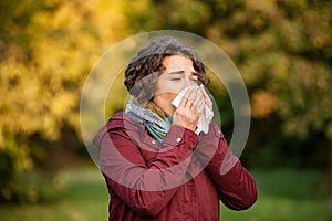 Woman in park sneezing and blowing nose