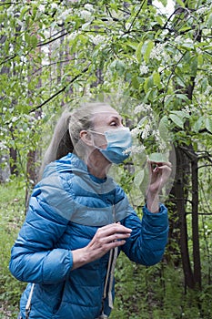 A woman in a park sniffs a bird cherry in a protective mask on her face