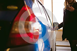 Woman in parking lot on blue car background. Opens door with key..