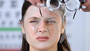 Woman with partly closed eyes, doctor putting phoropter on patients face, vision