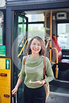 Woman passenger with backbag getting off the bus in vacation