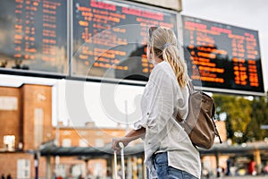 Woman passenger is checking arrival and departure board schedule timetable at train or bus station